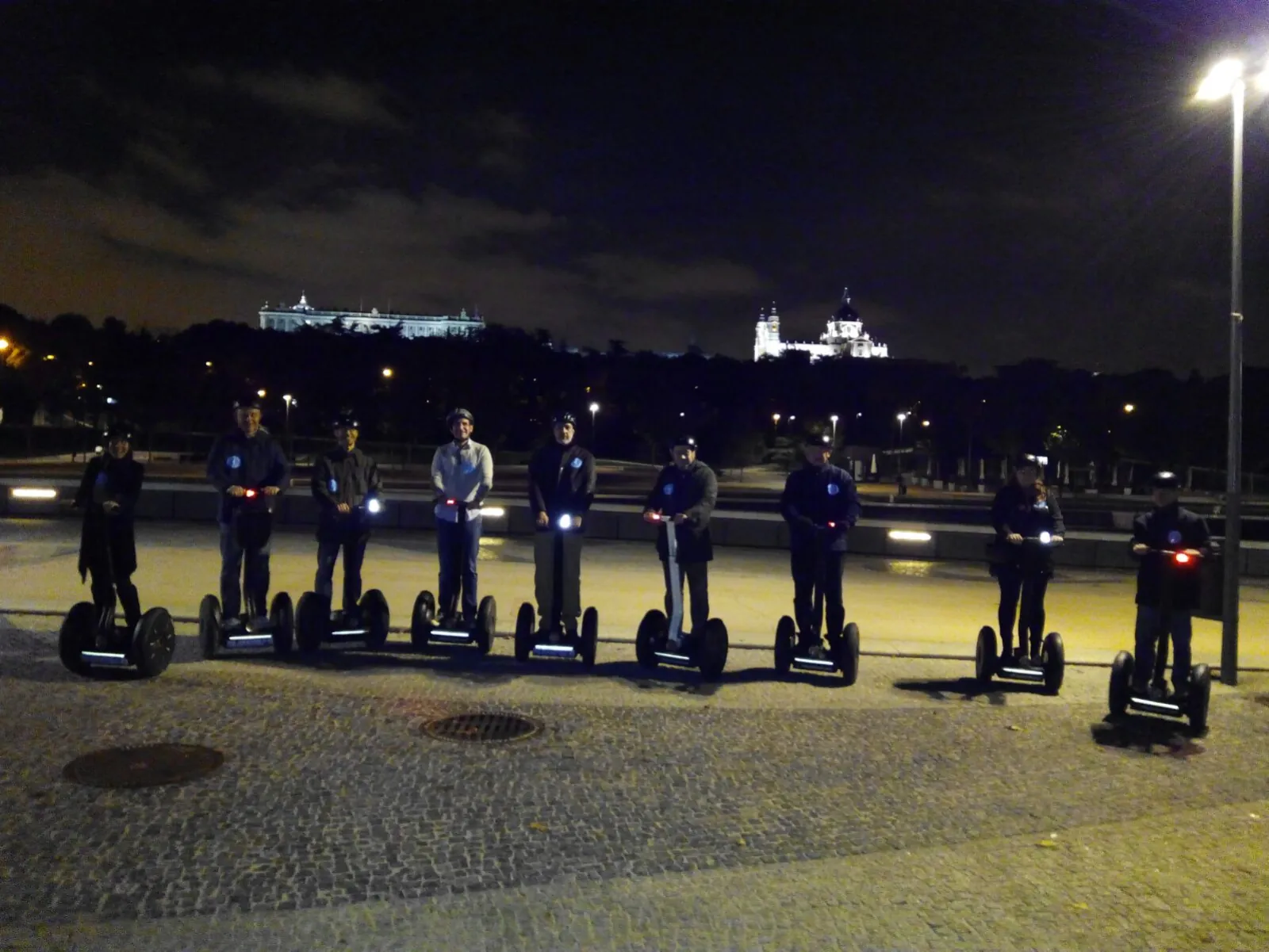 Riders on Segways on a floodlit Madrid riverside at night